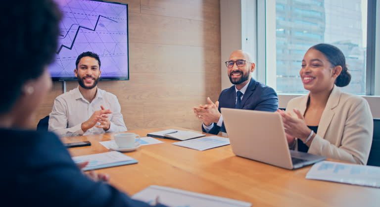 A group of business people discuss potential acquisitions around a conference table.