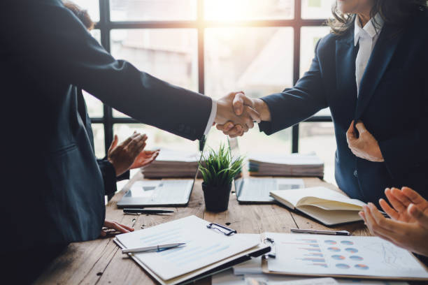 A businessman shakes hands with a businesswoman over a merger. 